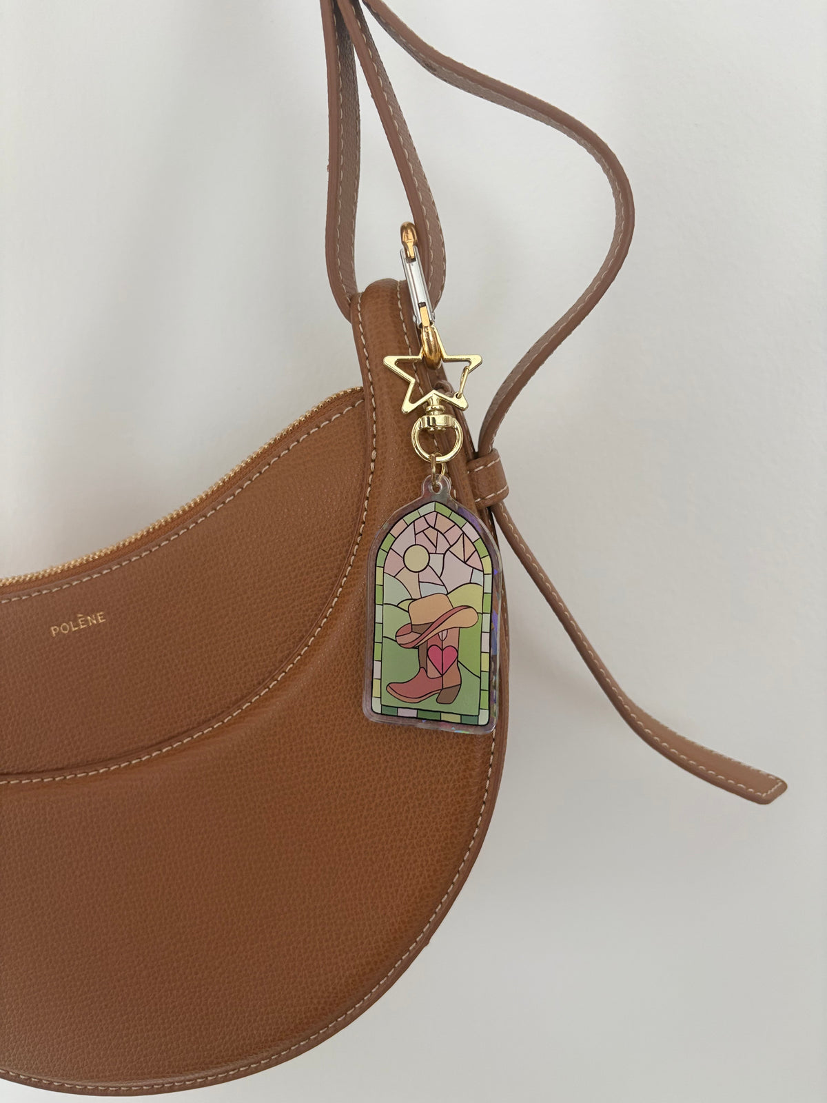 Stained glass style acrylic keychain with a character in a hat on a brown Polène handbag