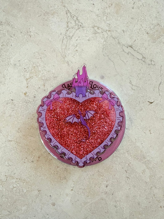 A heart shaped kindle and phone grip with a glittery pink center, purple dragon and flame illustrations, and a pink ruffled border.
