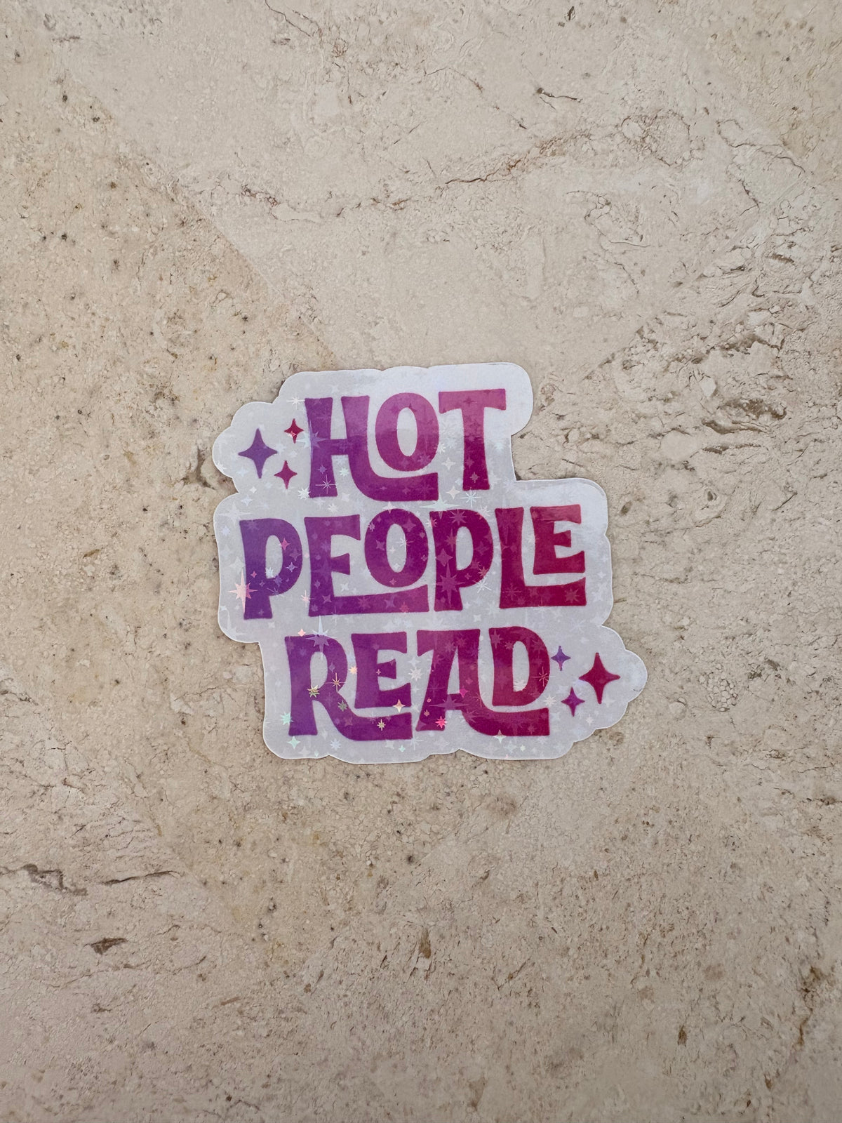 Purple gradient sticker with text 'HOT PEOPLE READ' and stars on a stone surface.