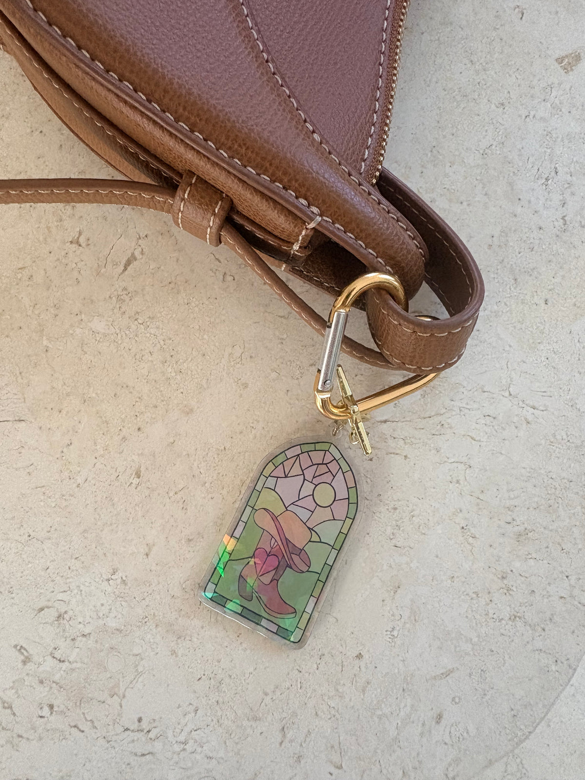 Stained glass style holographic acrylic keychain attached to a brown leather bag