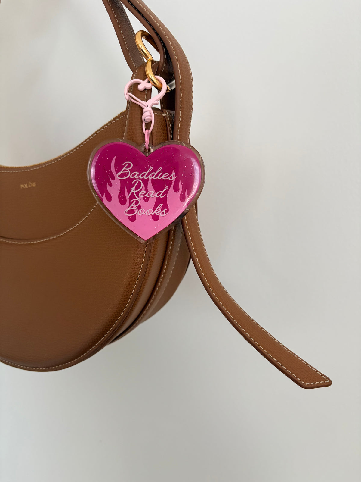 Heart-shaped acrylic keychain with 'Baddies Read Books' text attached to a brown leather handbag