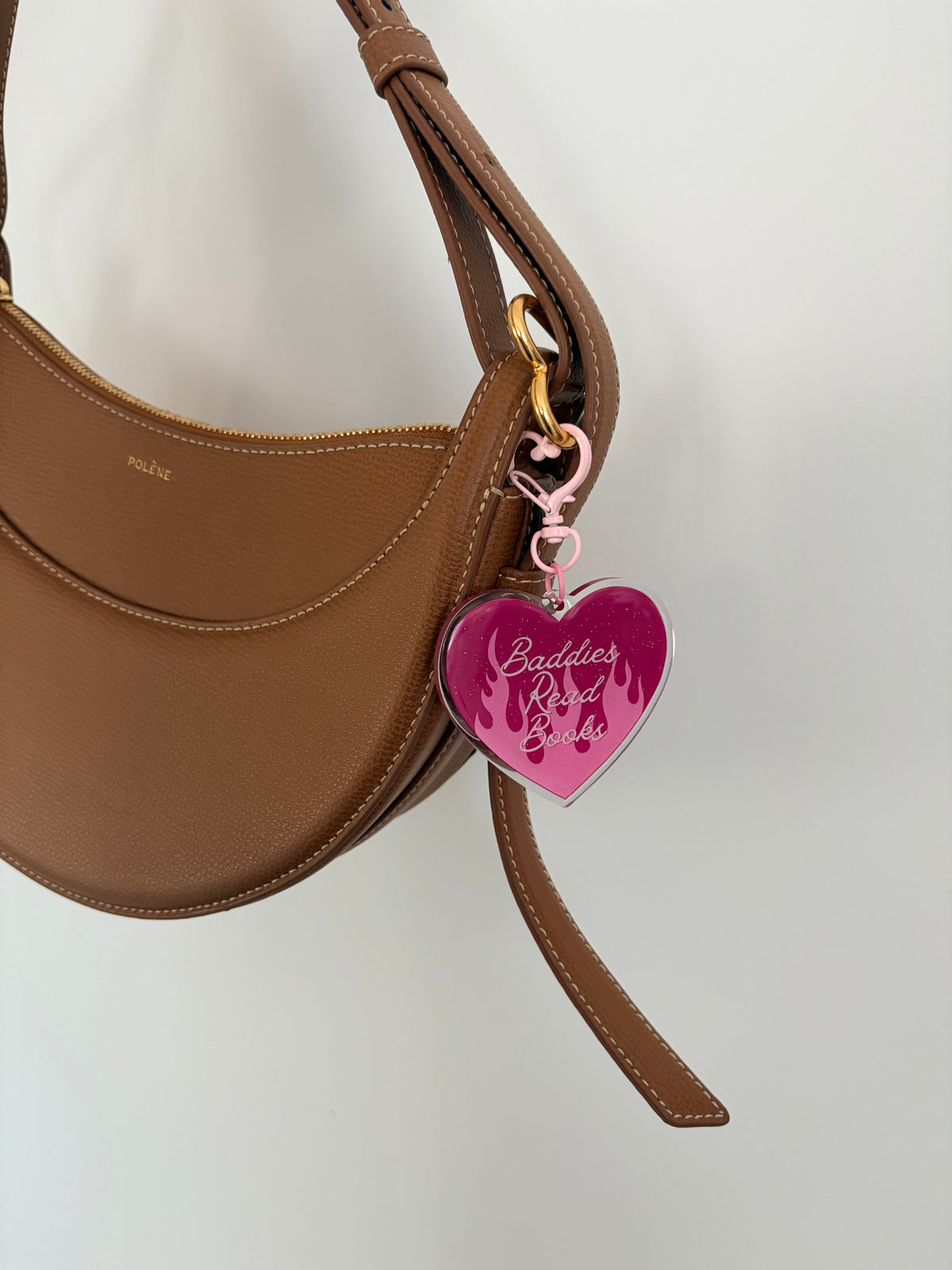 Heart-shaped pink acrylic keychain with 'Baddies Read Books' text on a brown leather handbag