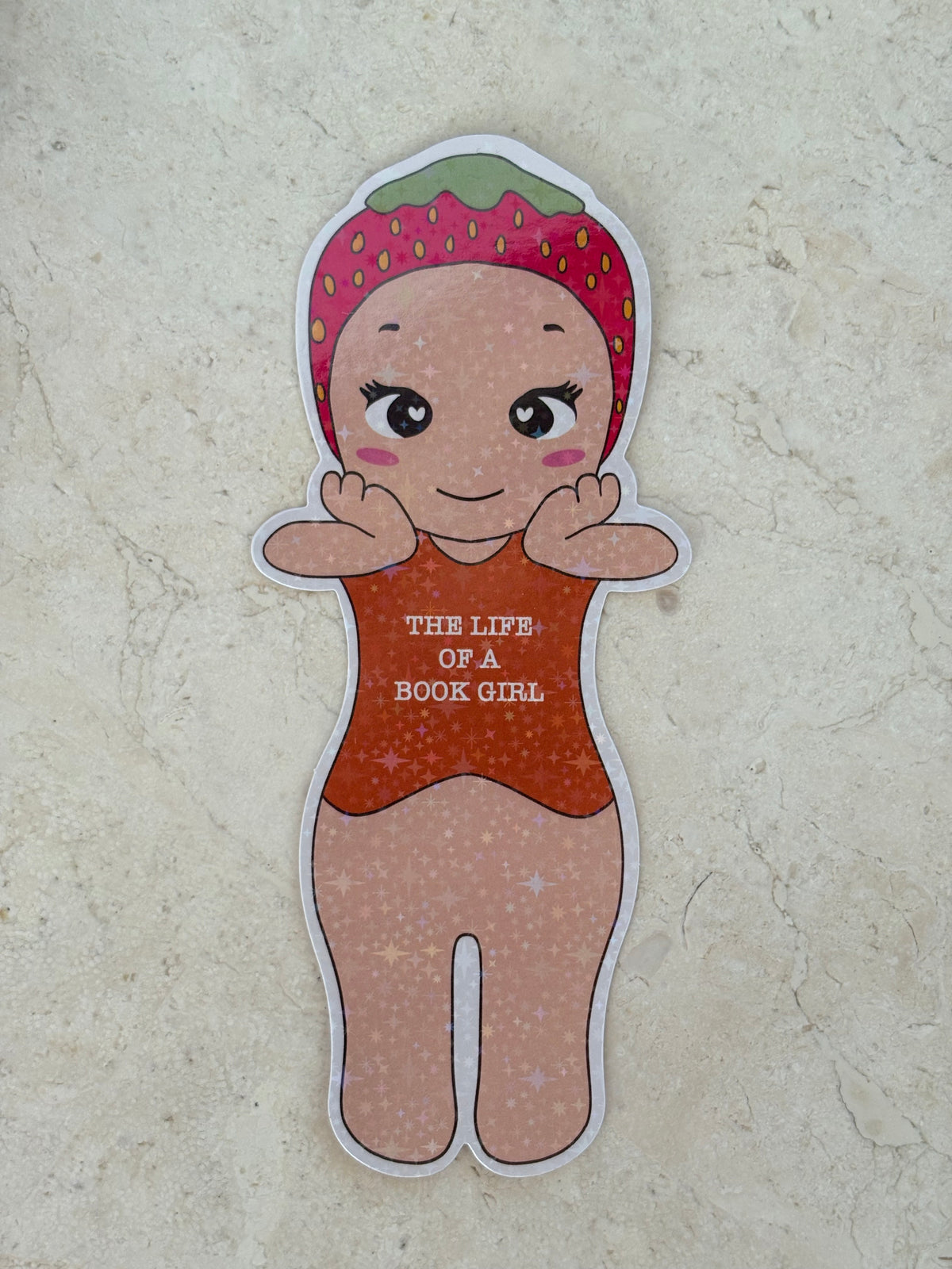 Die-cut sticker of a girl wearing a strawberry hat and orange outfit saying THE LIFE OF A BOOK GIRL