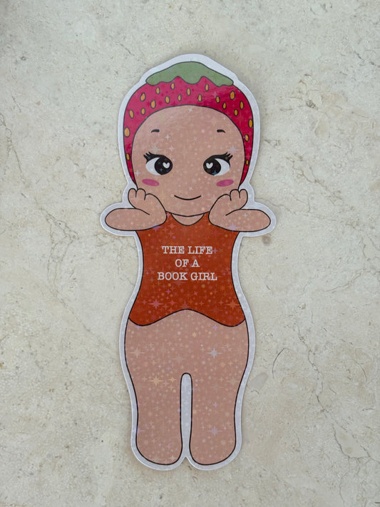 Die-cut sticker of a girl wearing a strawberry hat and orange outfit saying THE LIFE OF A BOOK GIRL