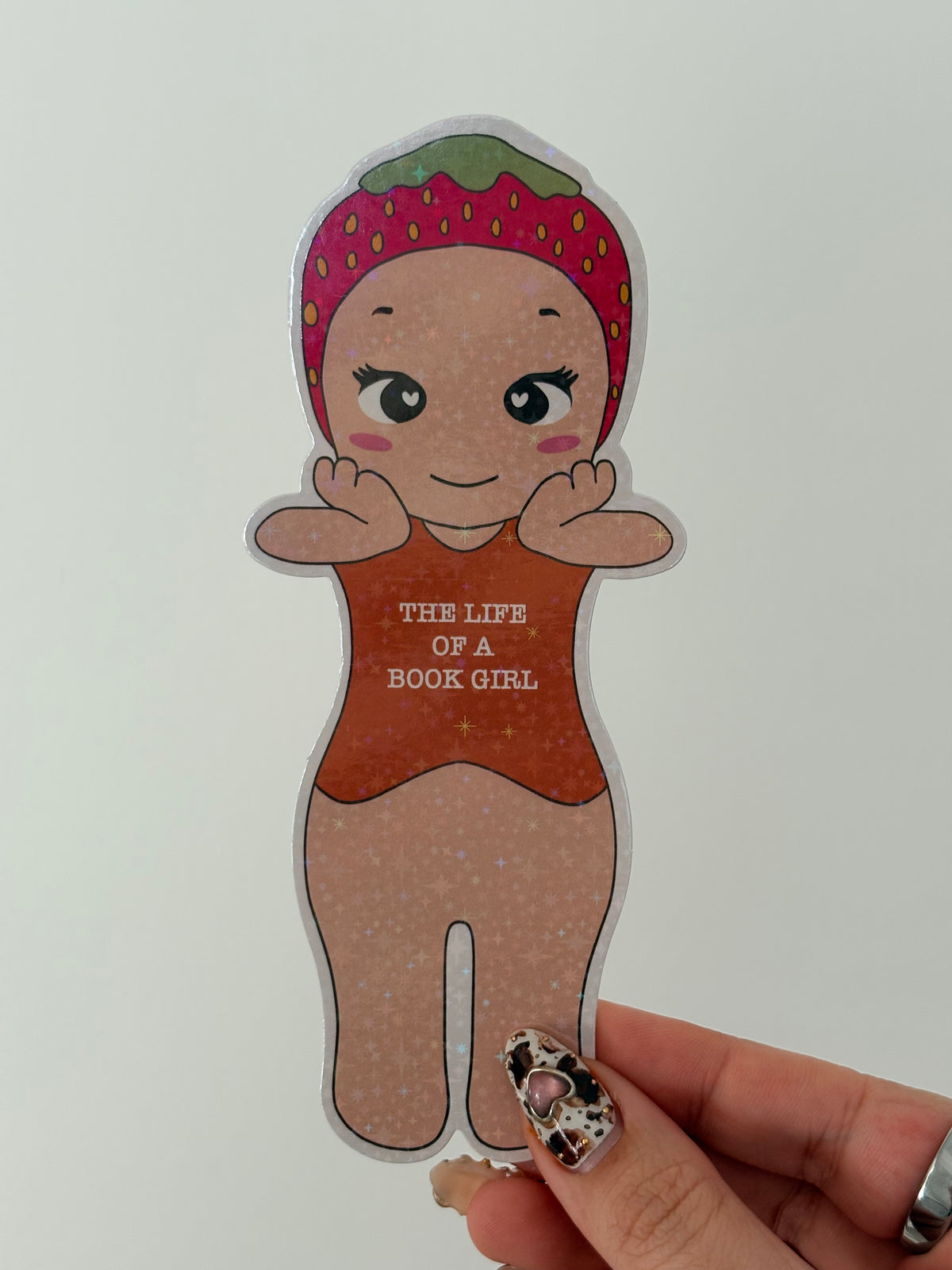 Die-cut sticker of a cute girl wearing a strawberry hat and a bodysuit saying The Life of a Book Girl