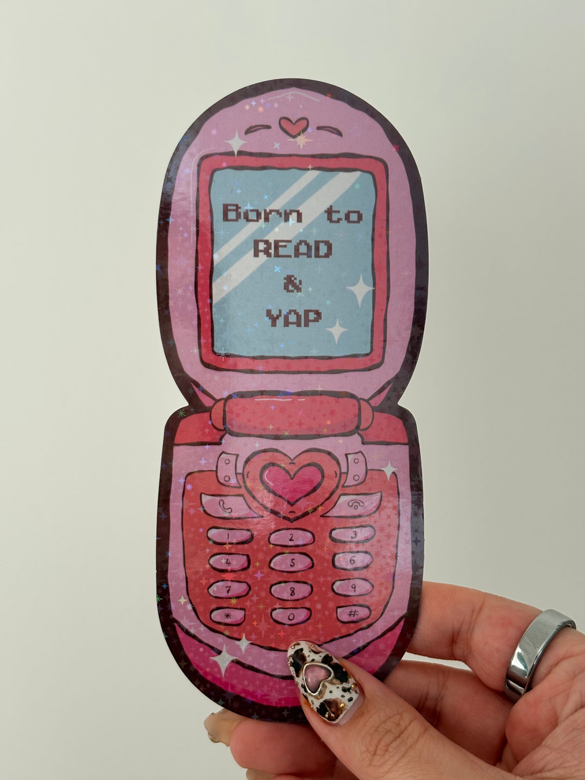 Pink holographic flip phone sticker with 'Born to READ & YAP' text on a pixelated screen.