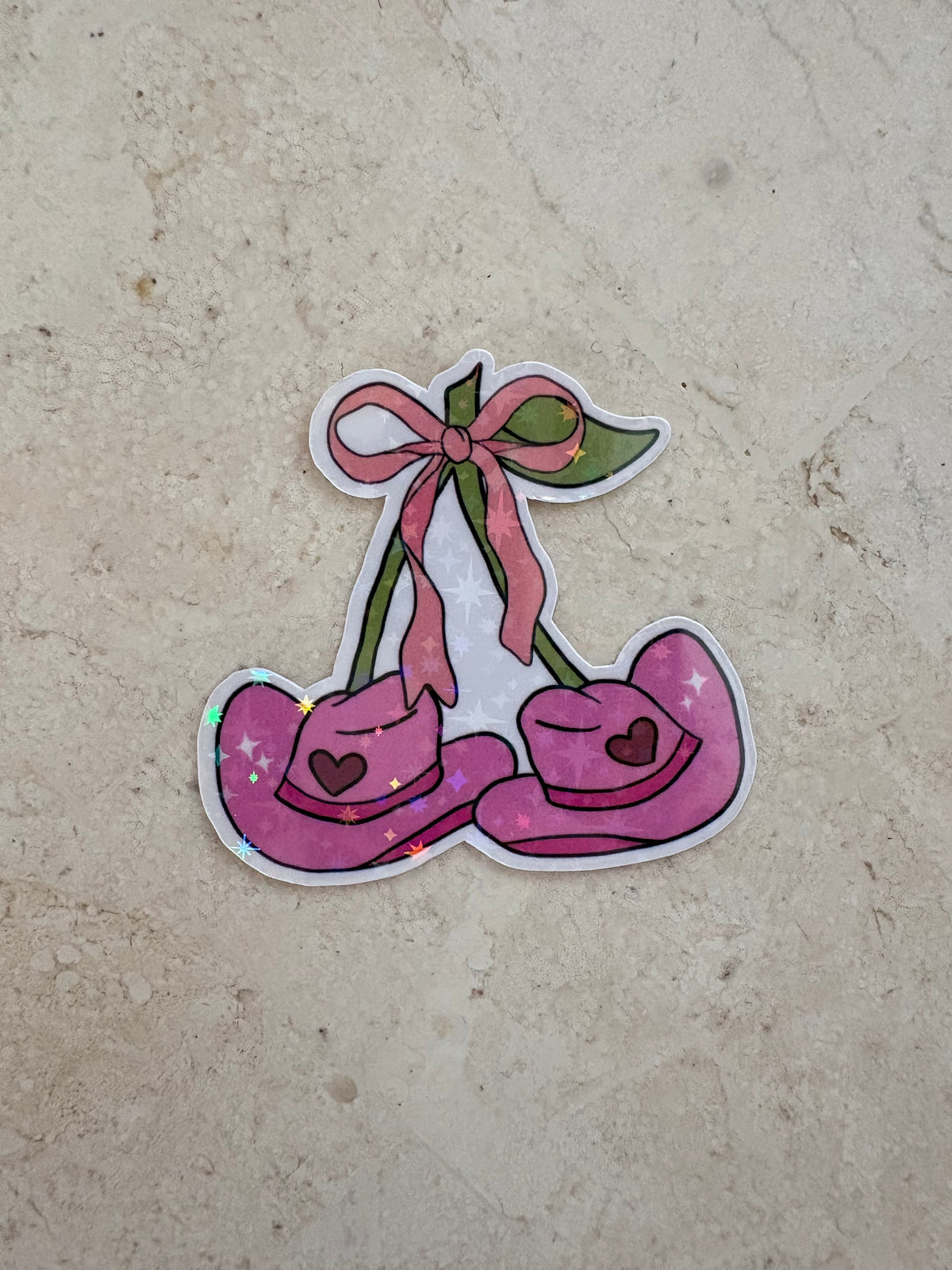 Holographic sticker of pink cowboy hats shaped like cherries with a pink bow.