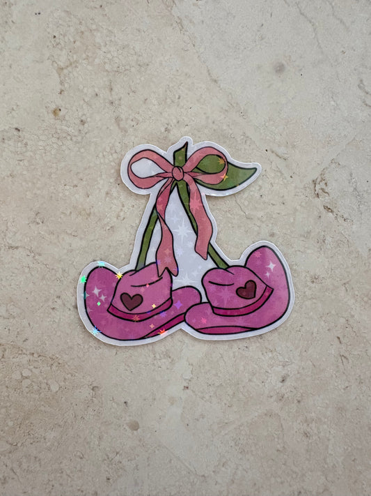 Holographic sticker of pink cowboy hats shaped like cherries with a pink bow.