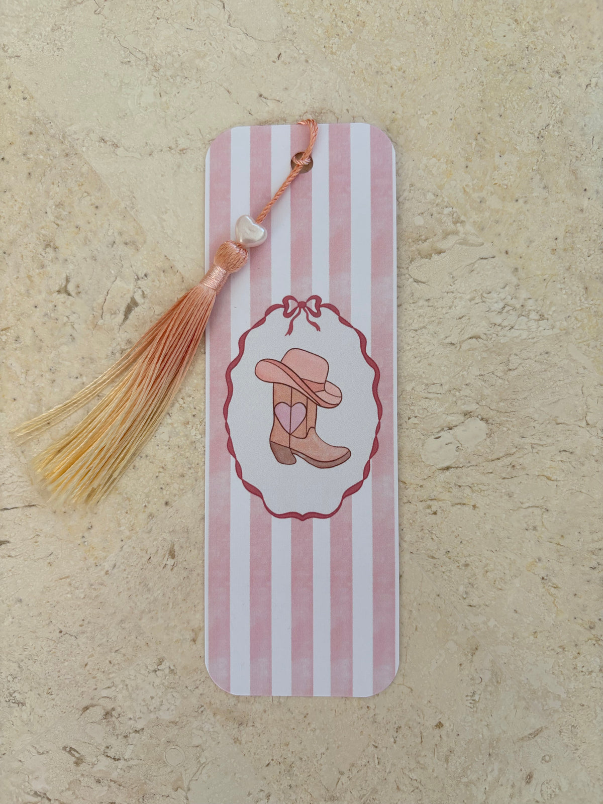Pink and white striped bookmark with a cowgirl boot illustration and orange tassel
