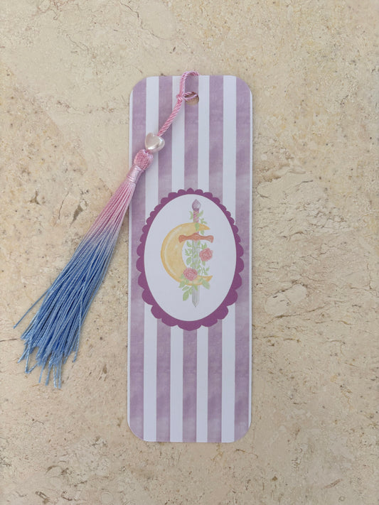 Purple and white striped bookmark with a crescent moon, sword, and pink-to-blue tassel.